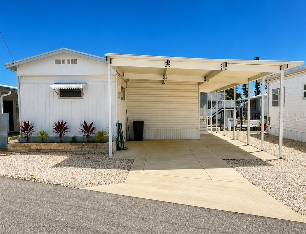 A white mobile home with a carport and a small landscaped garden bed — 6918 E BAYOU LANE, BRADENTON, FL