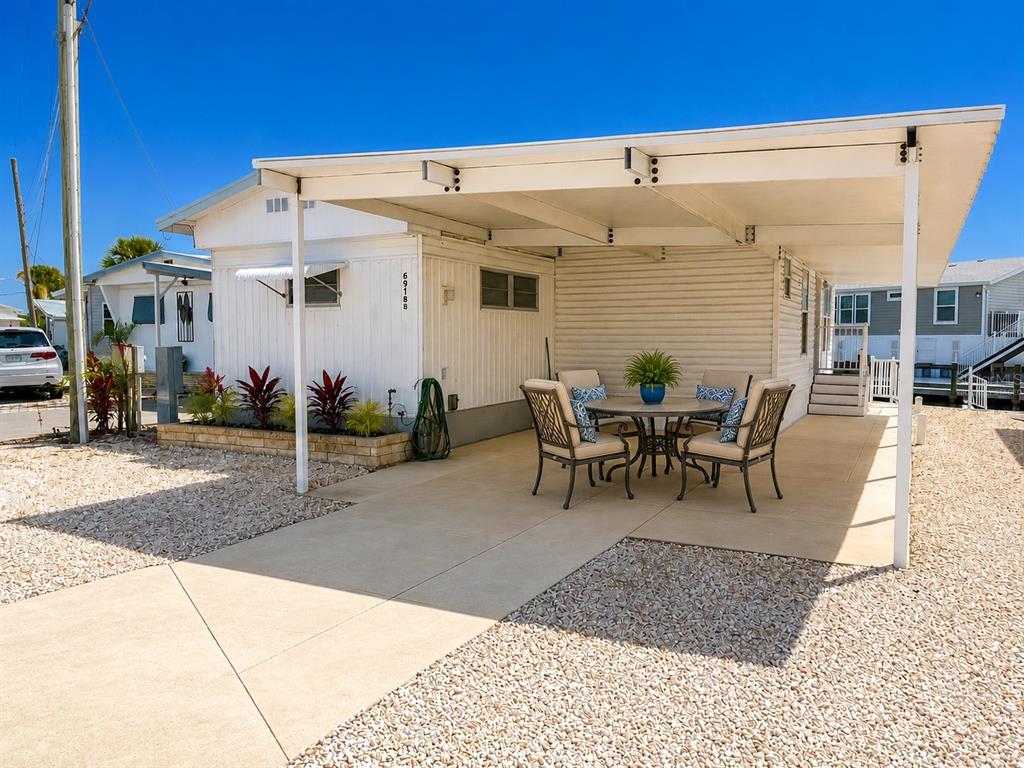A mobile home exterior features a covered concrete patio with outdoor furniture and gravel landscaping — 6918 E BAYOU LANE, BRADENTON, FL