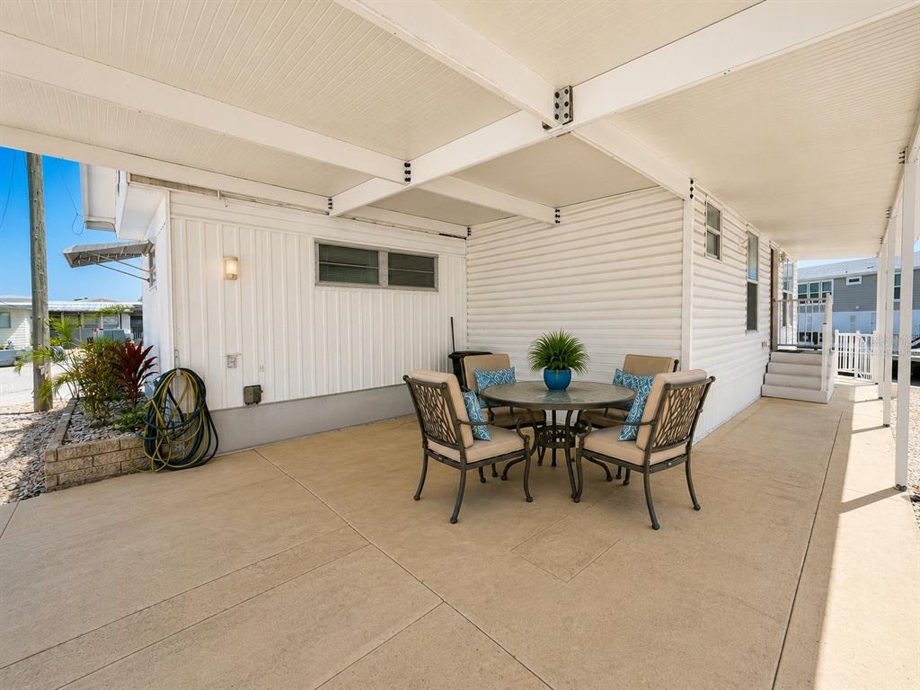A covered patio features a round dining table with four chairs against a white house — 6918 E BAYOU LANE, BRADENTON, FL