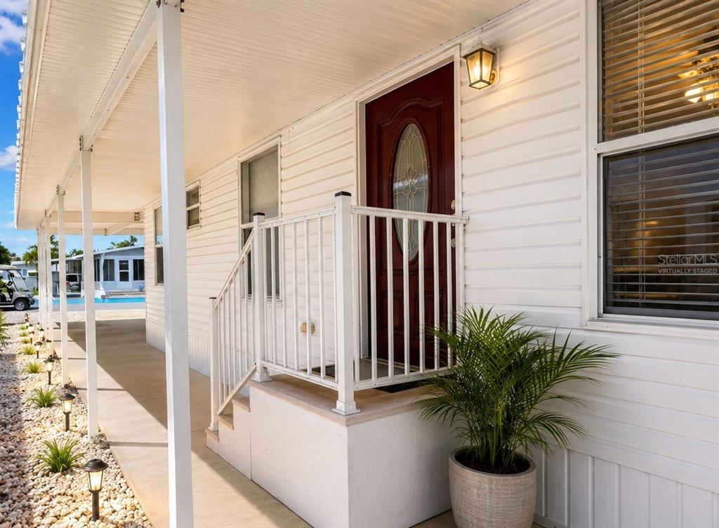 A white mobile home exterior features a red front door, porch railing, and gravel landscaping — 6918 E BAYOU LANE, BRADENTON, FL