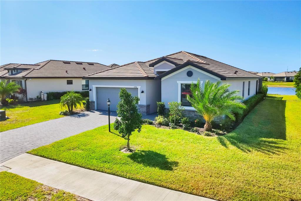 A single-story suburban house with a gray exterior, tiled roof, and a paved driveway — 15716 BAREFOOT BEACH DRIVE, BRADENTON, FL