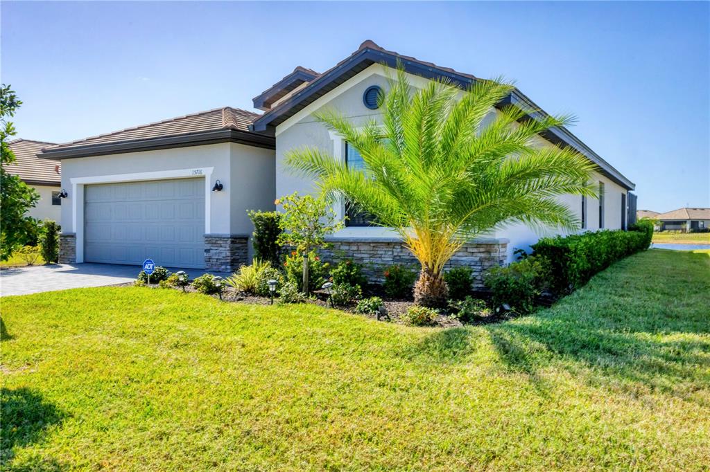 A single-story house with a gray garage, stone accents, and a palm tree in front — 15716 BAREFOOT BEACH DRIVE, BRADENTON, FL