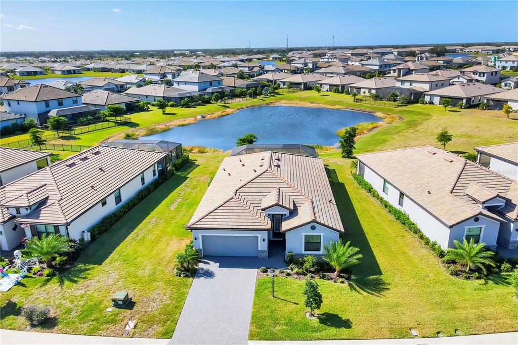 An aerial view shows a single-story suburban house with a tiled roof and driveway — 15716 BAREFOOT BEACH DRIVE, BRADENTON, FL