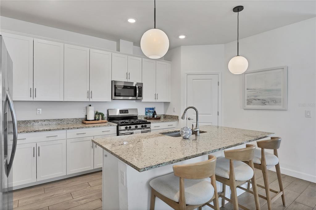 A kitchen features white cabinets, granite countertops, a center island with stools, and pendant lighting — 15716 BAREFOOT BEACH DRIVE, BRADENTON, FL