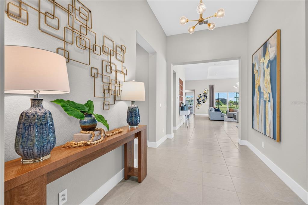 A bright entryway features a wooden console table, blue lamps, and geometric wall art — 8154 REDONDA LOOP, LAKEWOOD RANCH, FL