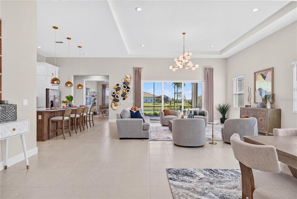 An open-concept living area features a kitchen with bar seating, neutral furniture, and large windows — 8154 REDONDA LOOP, LAKEWOOD RANCH, FL