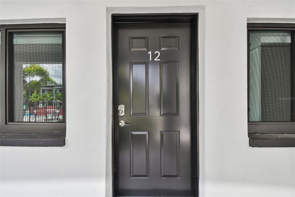 A black front door with the number 12 is centered between two windows on a wall — 2942 W BAY DRIVE UNIT 2, BELLEAIR BLUFFS, FL