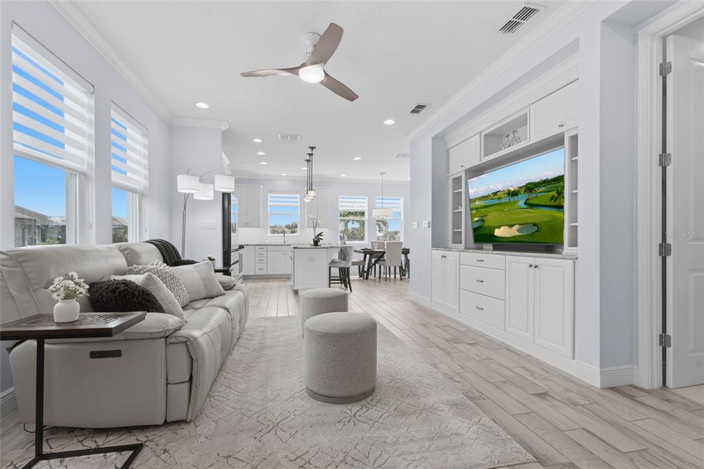 A bright open-concept living room features a white sofa, built-in media center, and kitchen area — 5353 BENTGRASS WAY, LAKEWOOD RANCH, FL