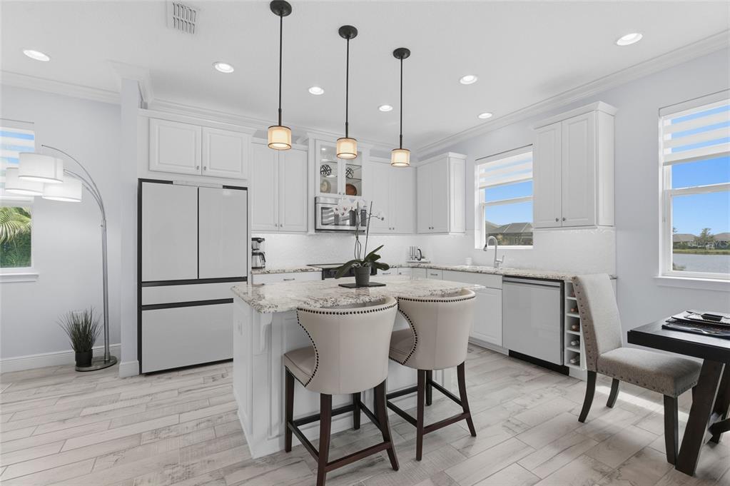 A bright kitchen features white cabinets, a granite-topped island, pendant lighting, and light wood flooring — 5353 BENTGRASS WAY, LAKEWOOD RANCH, FL