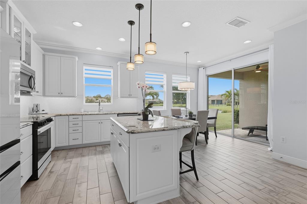 A bright kitchen features white cabinets, a granite island, and a dining area with patio access — 5353 BENTGRASS WAY, LAKEWOOD RANCH, FL