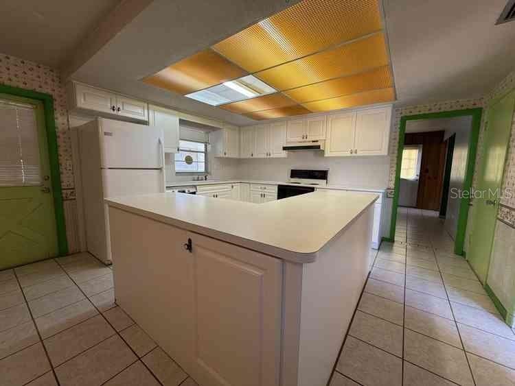 A kitchen features white cabinets, a peninsula, tile flooring, and a large drop ceiling light — 3355 WILLIS ROAD, MULBERRY, FL