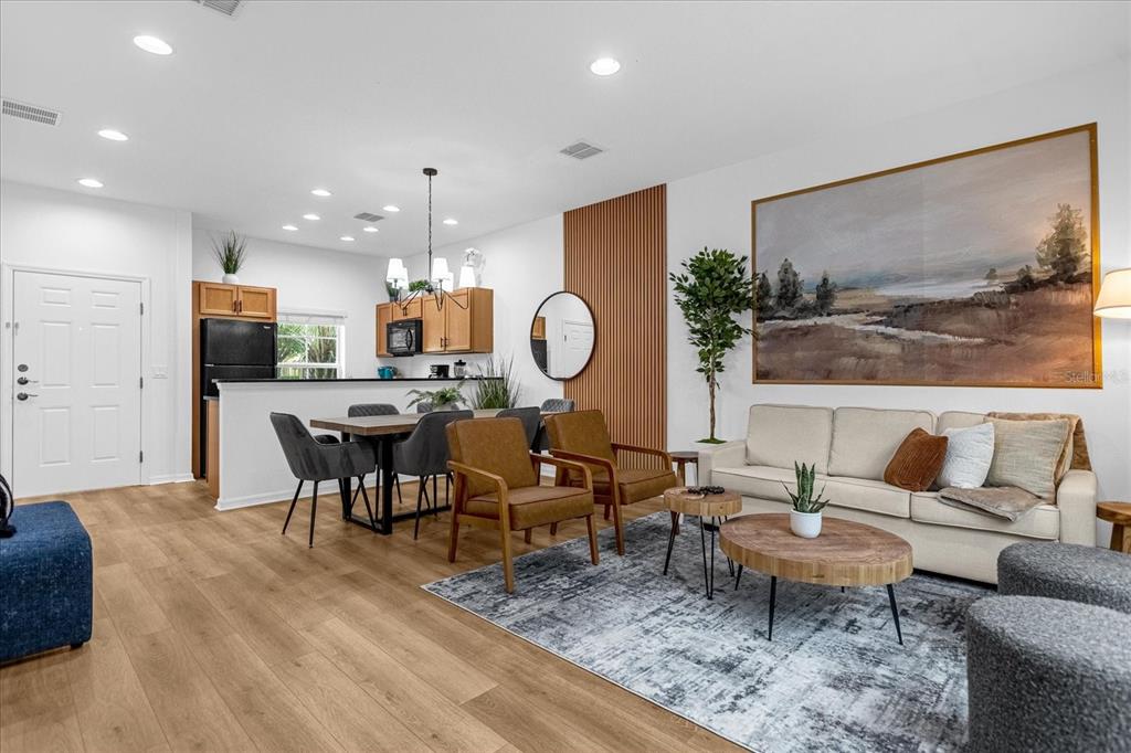 An open-concept living and dining area features wood-look flooring, a kitchen island, and modern decor — 3054 YELLOW LANTANA LANE, KISSIMMEE, FL