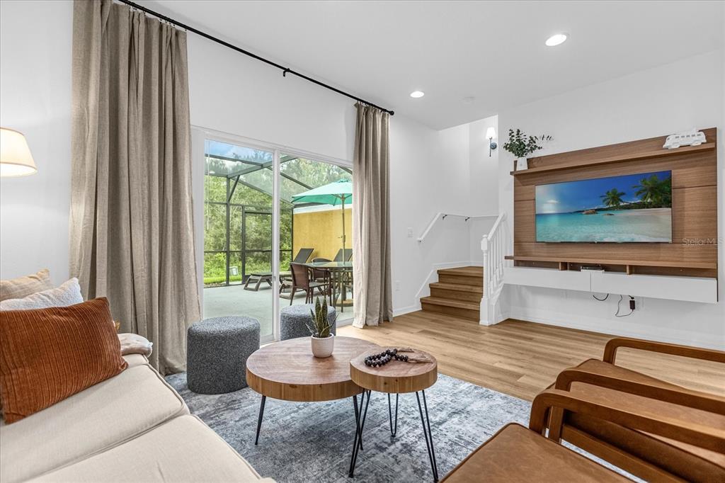 A living room features a wood-paneled media wall, sliding glass doors, and stairs leading upward — 3054 YELLOW LANTANA LANE, KISSIMMEE, FL