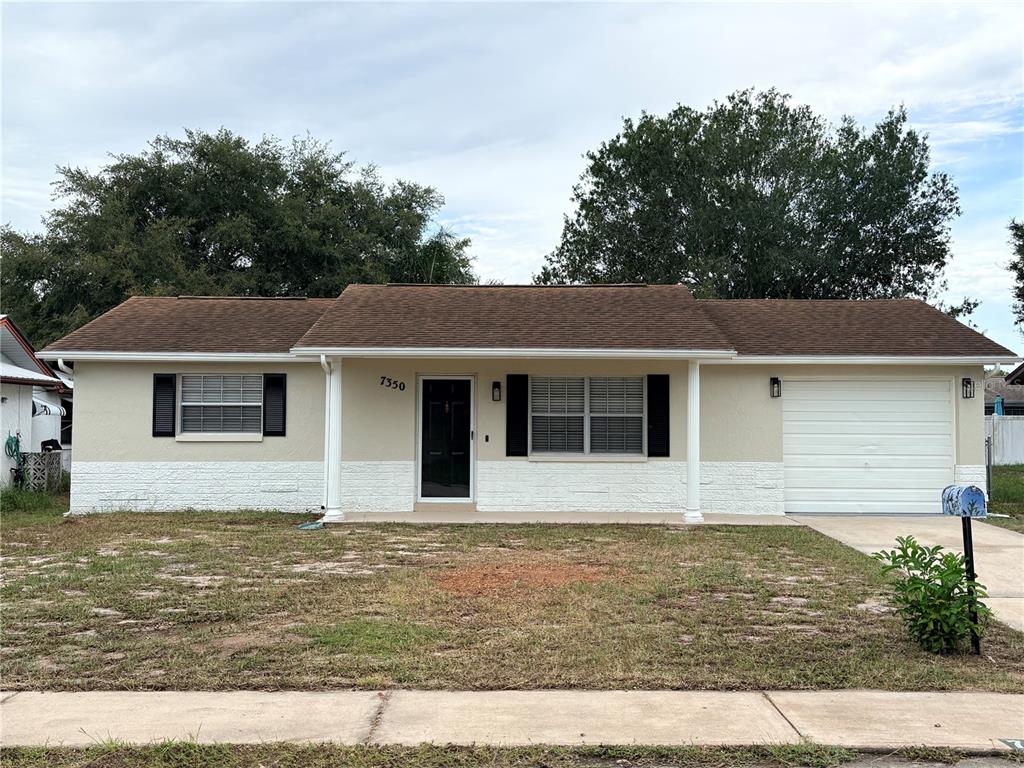 A single-story house with a beige exterior, white stone base, dark shutters, and a garage — 7350 FAIRFAX DRIVE, PORT RICHEY, FL