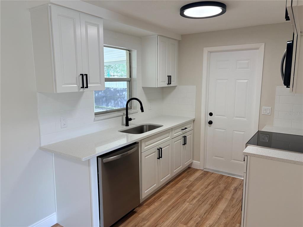 A kitchen features white cabinets, quartz countertops, a stainless steel dishwasher, and a black faucet — 7350 FAIRFAX DRIVE, PORT RICHEY, FL