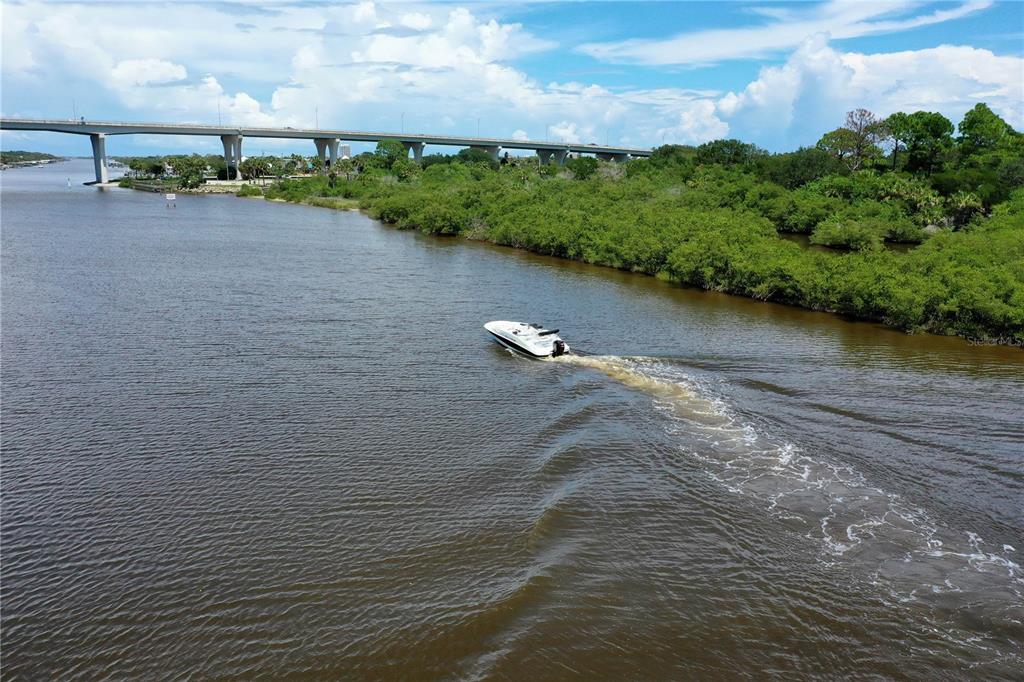 A white motorboat travels on a river beneath a large concrete bridge — 89 CORONADO ROAD, FLAGLER BEACH, FL