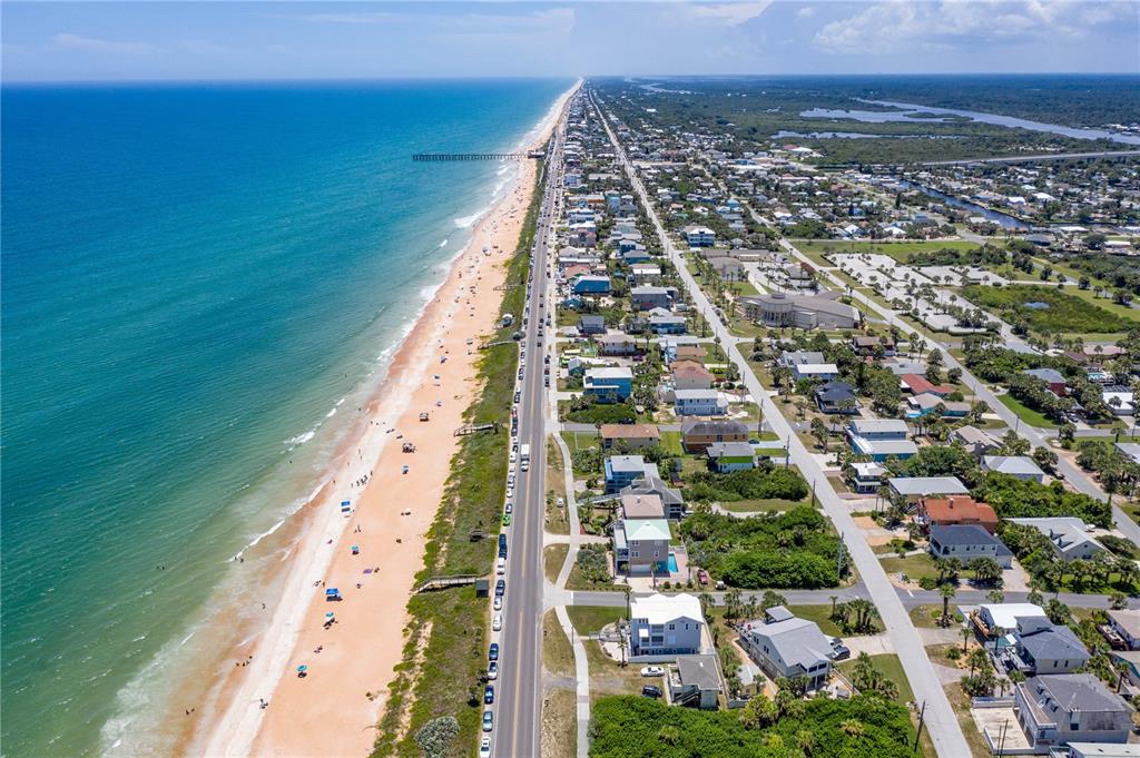 An aerial view shows a coastal town with a sandy beach, ocean, and residential homes — 89 CORONADO ROAD, FLAGLER BEACH, FL