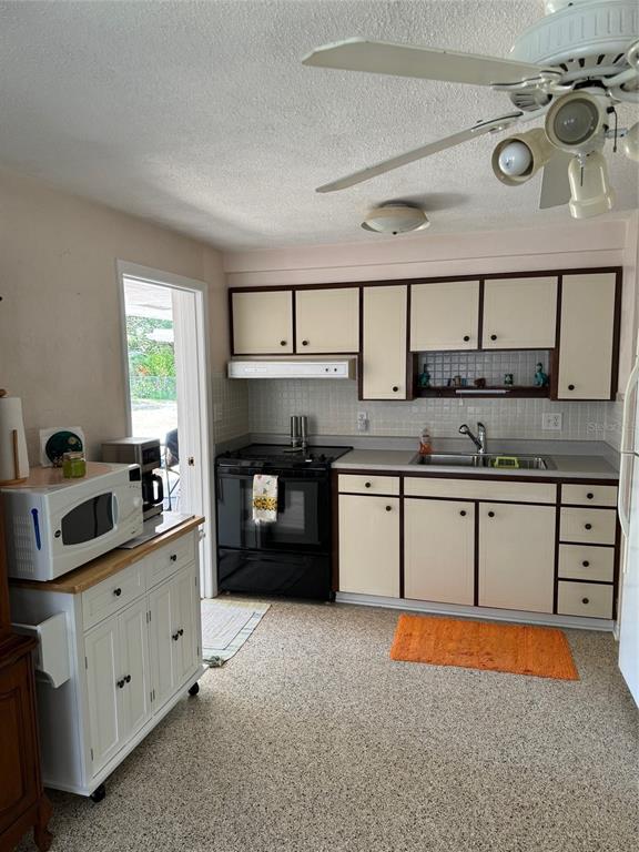 A kitchen features off-white cabinets, black appliances, a white rolling island, and speckled flooring — 814 E 10th AVENUE, NEW SMYRNA BEACH, FL
