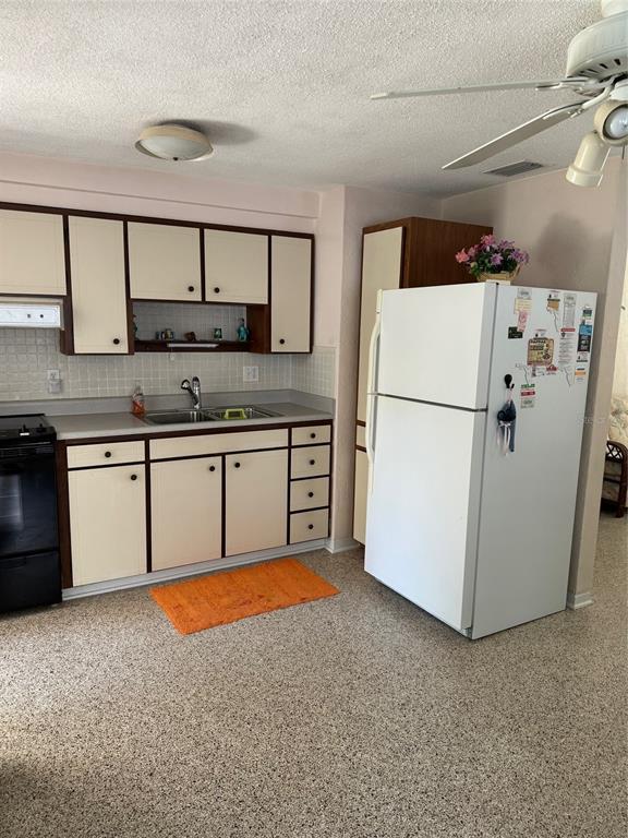 A kitchen features off-white cabinets with dark trim, a white refrigerator, and speckled flooring — 814 E 10th AVENUE, NEW SMYRNA BEACH, FL