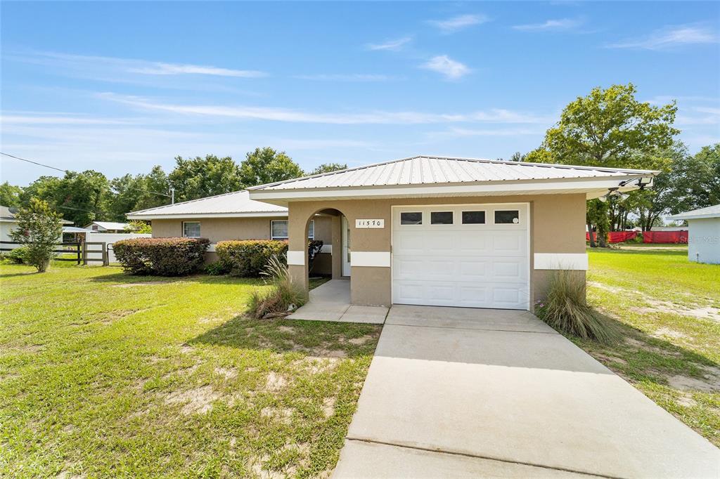 A single-story house with a tan stucco exterior, a metal roof, and a one-car garage — 11570 SE 84TH AVENUE, BELLEVIEW, FL