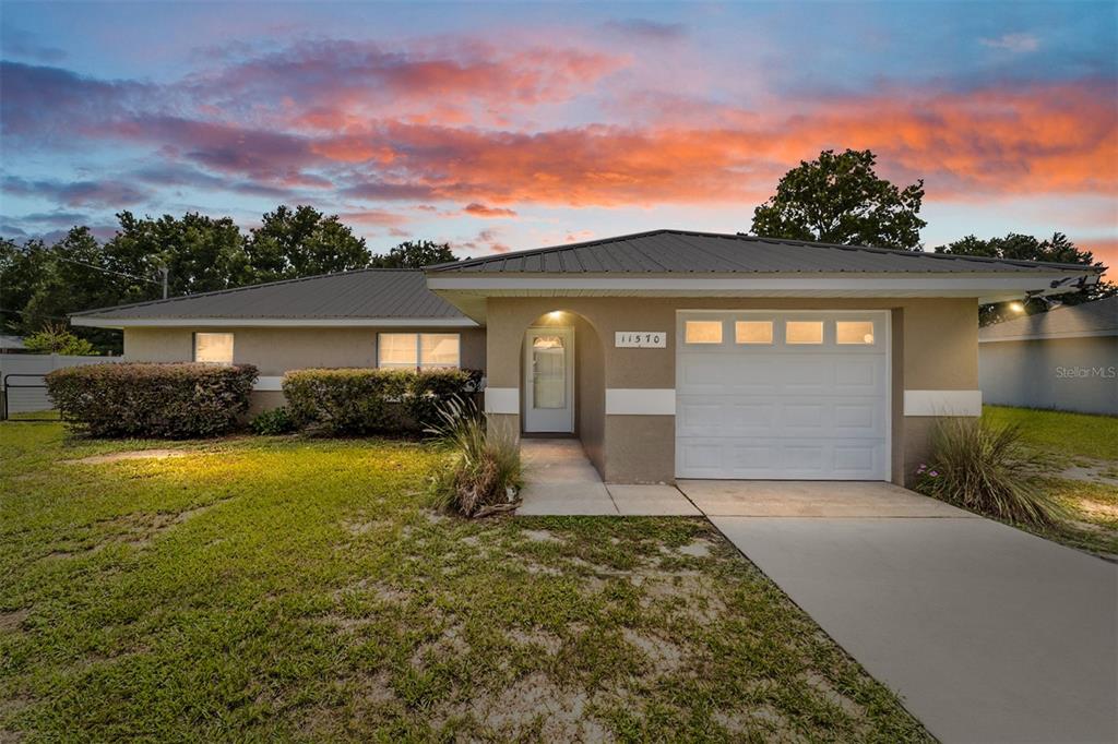 A single-story house with a metal roof, tan stucco exterior, and an attached garage — 11570 SE 84TH AVENUE, BELLEVIEW, FL