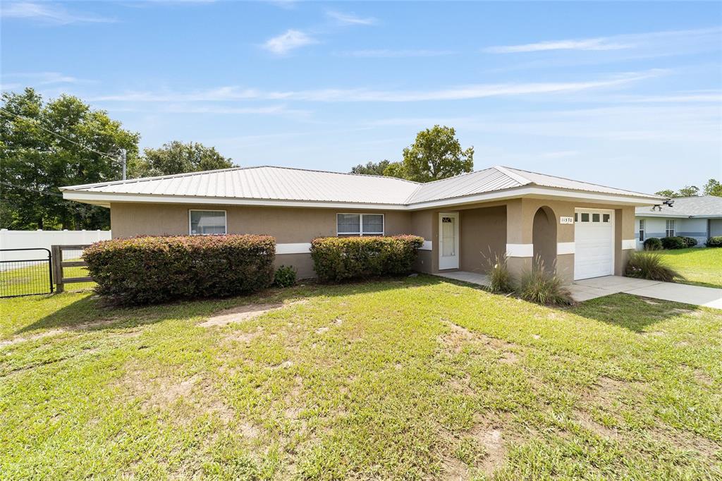 A single-story house with a metal roof, tan stucco exterior, and an attached garage — 11570 SE 84TH AVENUE, BELLEVIEW, FL
