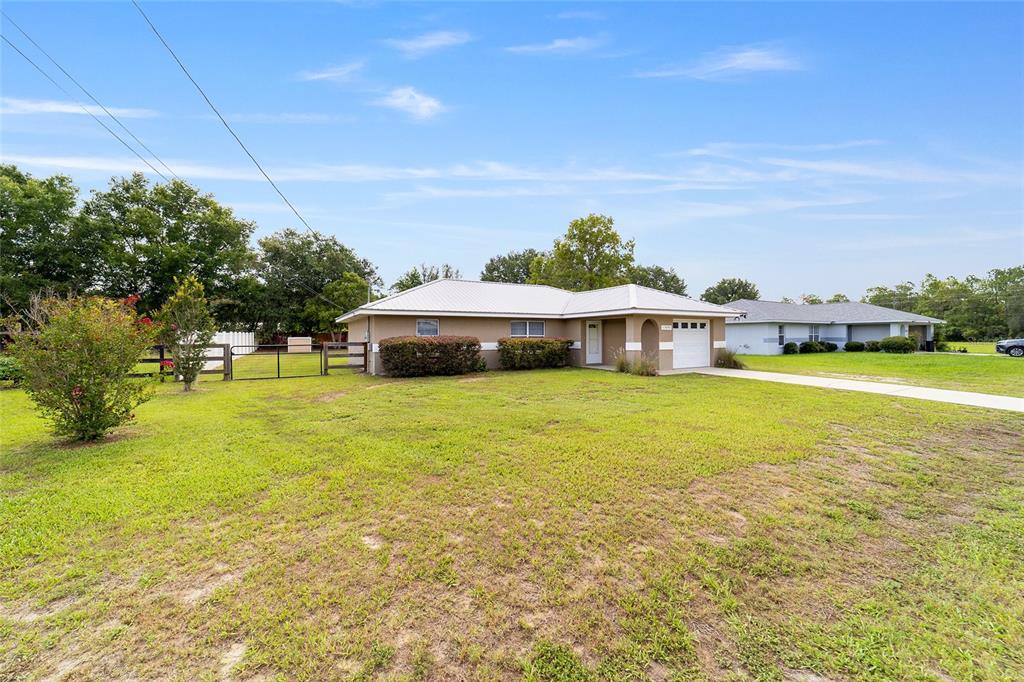 A single-story house with a metal roof, attached garage, and a large front lawn — 11570 SE 84TH AVENUE, BELLEVIEW, FL