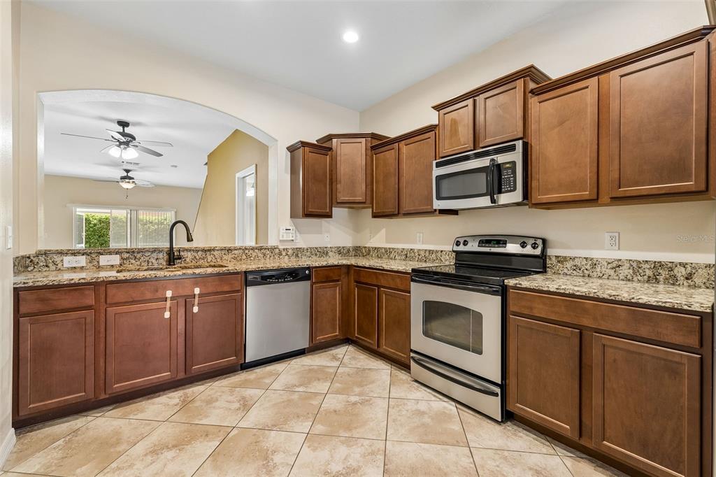A kitchen with wood cabinets, granite countertops, stainless steel appliances, and tile flooring — 4127 SHADE TREE LANE, LAKELAND, FL