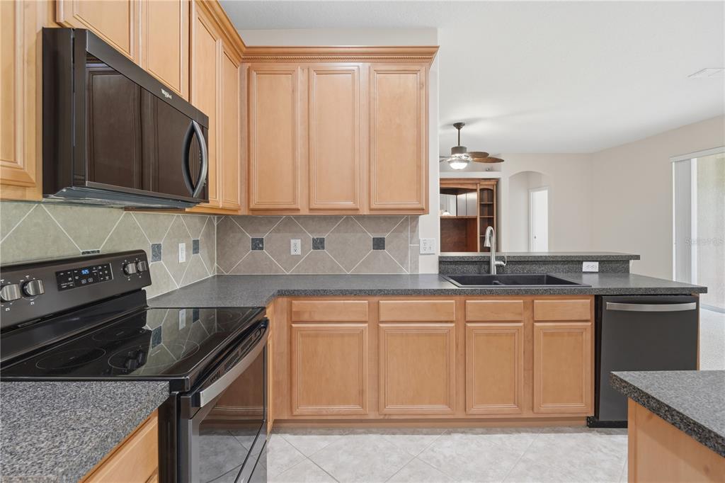 A kitchen features light wood cabinets, dark countertops, black appliances, and a tiled backsplash — 4203 ROCK HILL LOOP, APOPKA, FL