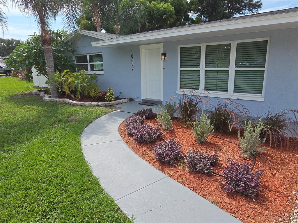 A light blue house features a curved concrete walkway leading to a white front door — 10827 VILLAGE GREEN AVENUE, SEMINOLE, FL