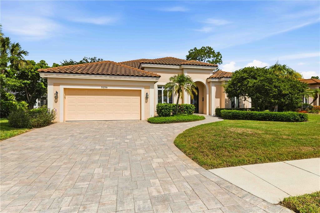 A paved walkway leads to the arched entryway of a tan stucco house with landscaping — 5256 E 88TH STREET, BRADENTON, FL