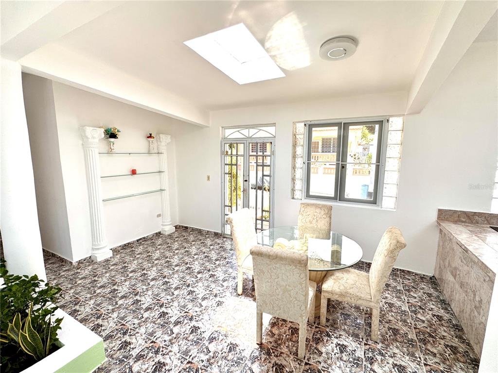 A dining area features a glass table, four chairs, tiled floors, and a skylight — 901 Mariani BO. EMAJAGÜAS, SECT MARIANI, MAUNABO, PR