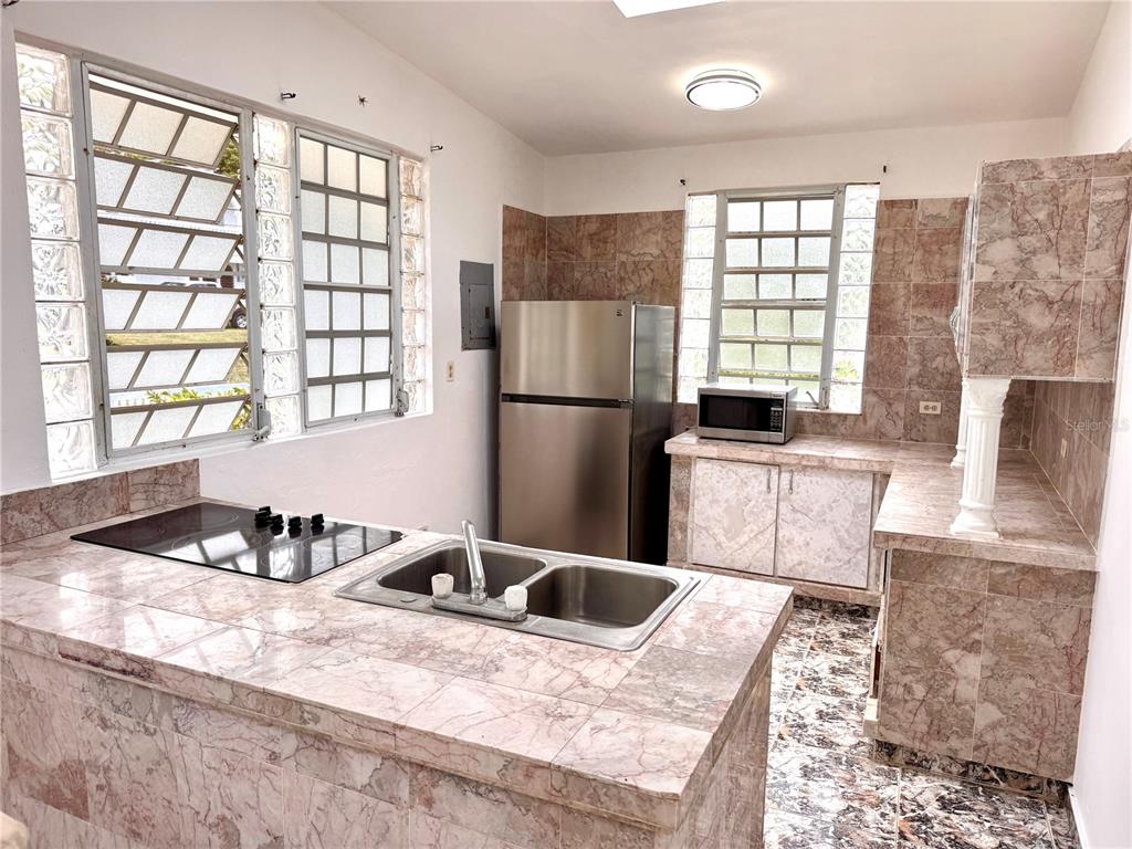 A kitchen features marble-tiled countertops, a stainless steel refrigerator, and glass block windows — 901 Mariani BO. EMAJAGÜAS, SECT MARIANI, MAUNABO, PR