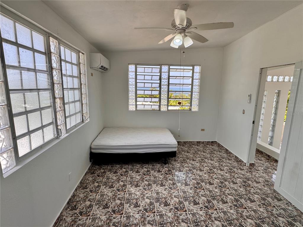 A bedroom features a mattress on a frame, tiled floors, a ceiling fan, and louvered windows — 901 Mariani BO. EMAJAGÜAS, SECT MARIANI, MAUNABO, PR