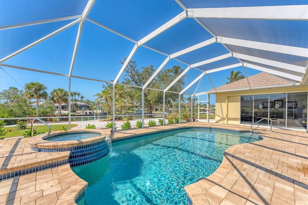 A screened-in pool and spa with paver decking overlooking a canal and palm trees — 285 SPANIARDS ROAD, PLACIDA, FL