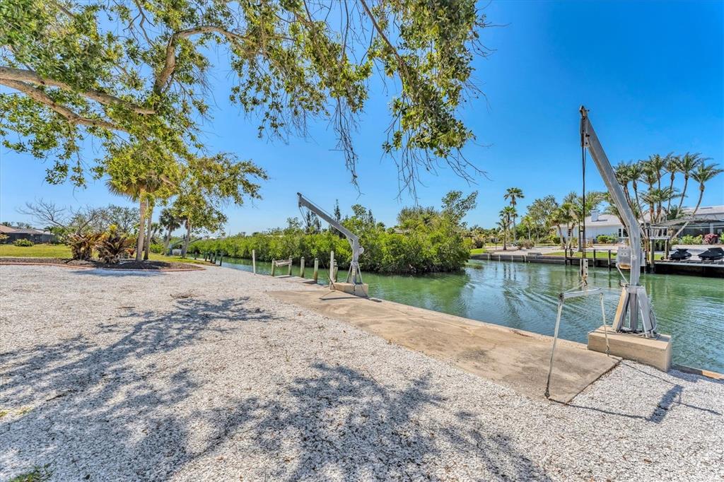 A gravel yard features two boat lifts along a concrete bulkhead overlooking a narrow canal — 285 SPANIARDS ROAD, PLACIDA, FL