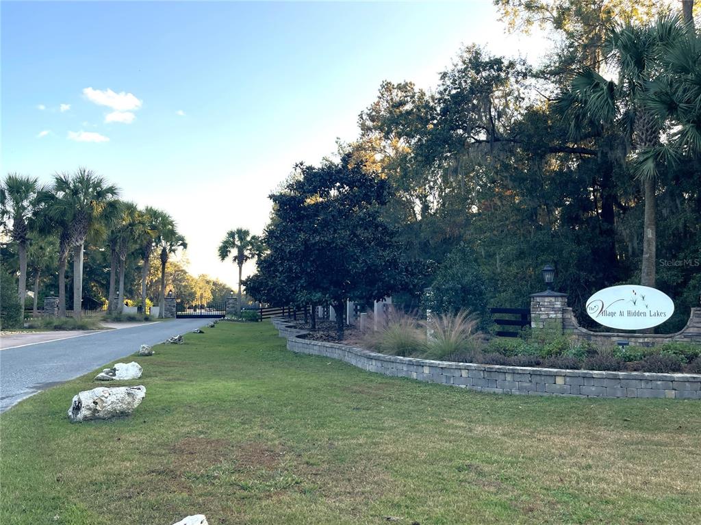 A stone wall and sign mark the entrance to a neighborhood with palm trees — NW 145TH AVE LOT 25, WILLISTON, FL