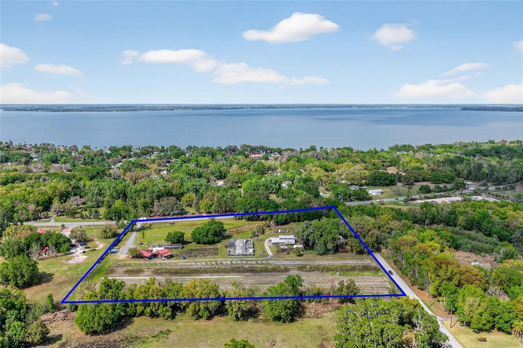 An aerial view shows a rectangular property with agricultural rows, outbuildings, and trees near water — CR 48, YALAHA, FL