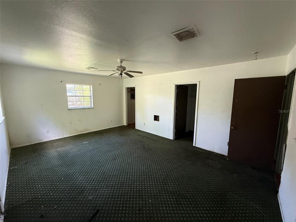 An empty room features dark patterned carpeting, white walls, a ceiling fan, and two doorways — 816 17TH COURT E, BRADENTON, FL