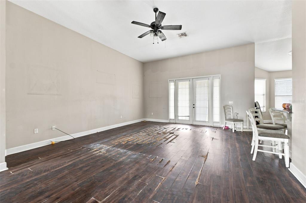 A living room with damaged dark wood flooring, beige walls, and a ceiling fan — 5598 THORNGROVE WAY, SPRING HILL, FL