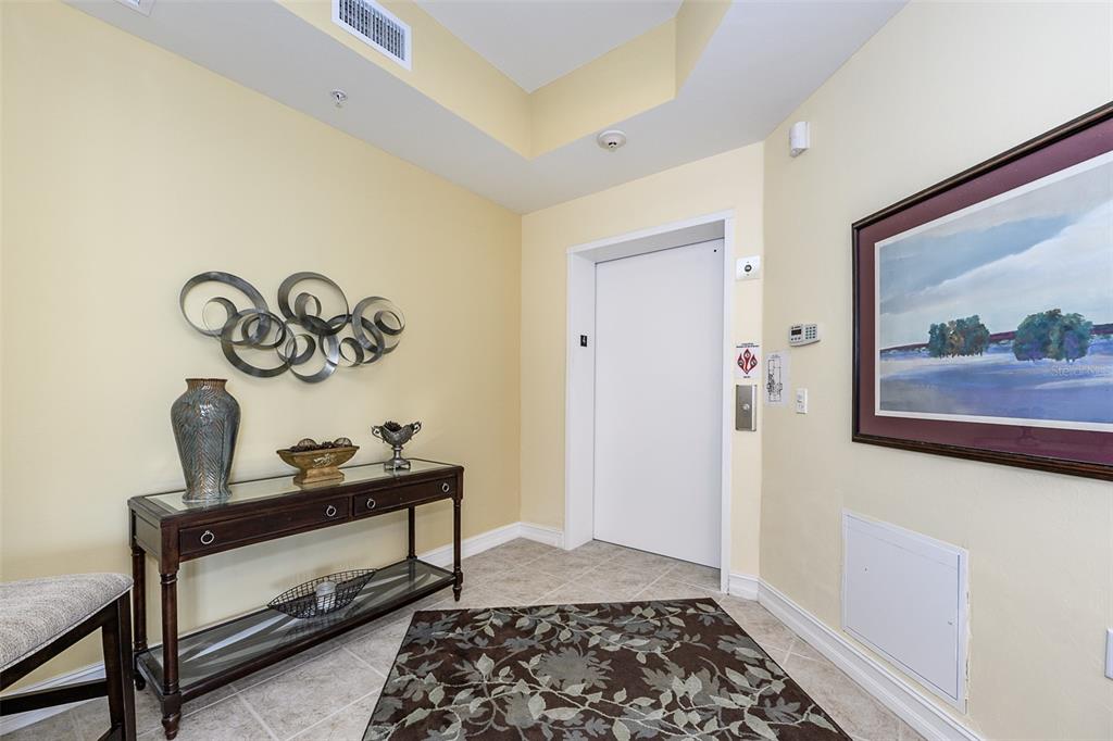 An elevator opens into a tiled foyer featuring a console table, wall art, and a rug — 85 VIVANTE BOULEVARD UNIT 8542, PUNTA GORDA, FL