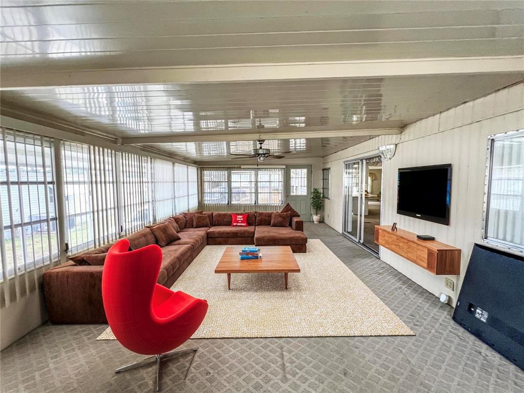 A sunroom features a large brown sectional sofa, a red egg chair, and a wall-mounted television — 326 MARTIN DRIVE, LAKELAND, FL