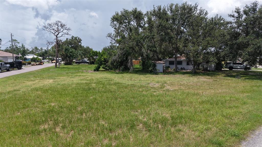A grassy, vacant residential lot is surrounded by mature trees and neighboring houses — 513 PINE ROAD, NOKOMIS, FL