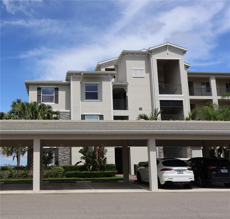 An exterior view of a multi-story stucco building with a tiled roof and palm tree — 920 TIDEWATER SHORES LOOP UNIT 301, BRADENTON, FL