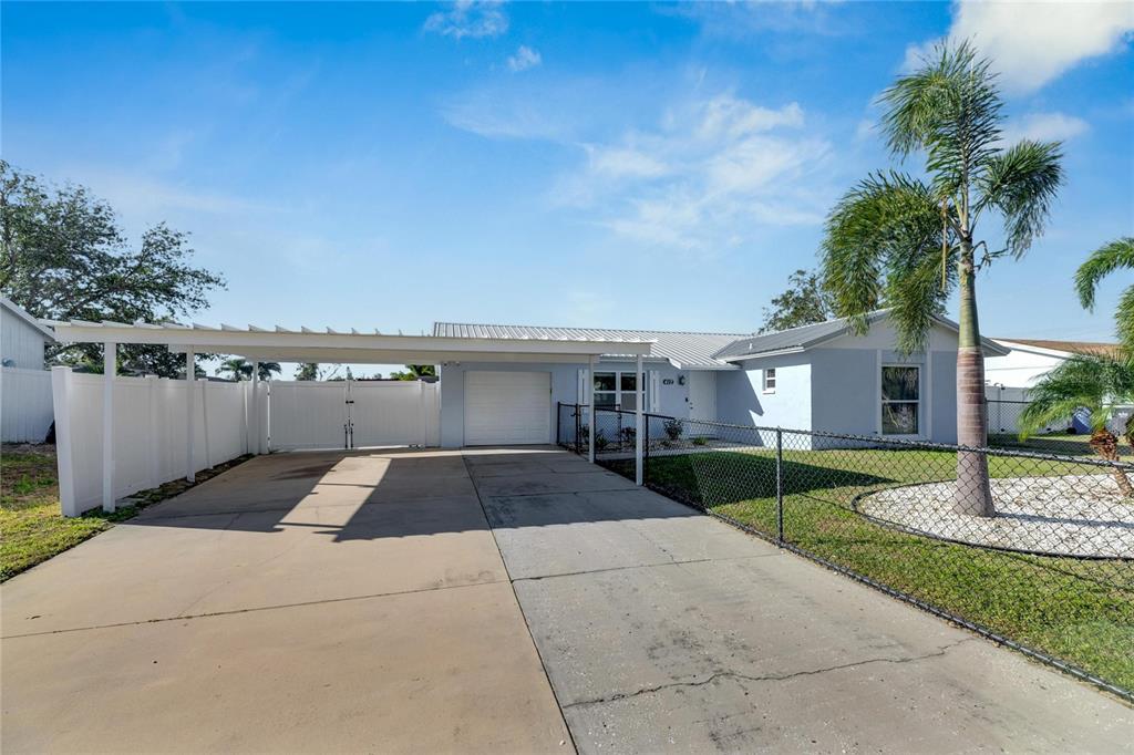 A light blue single-story house features a concrete driveway, a carport, and a chain-link fence — 412 FLAMINGO DRIVE, APOLLO BEACH, FL