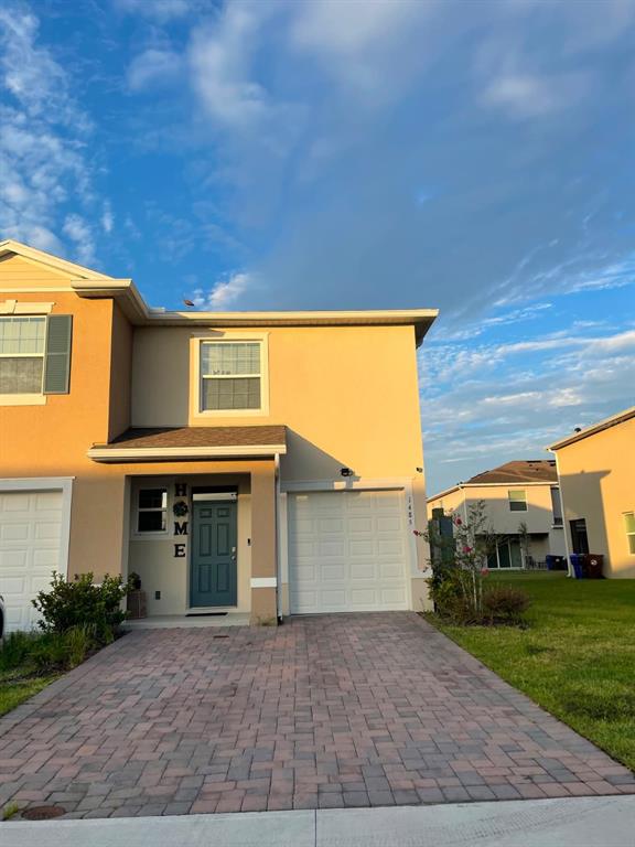 A two-story tan townhouse features a paved driveway, a garage, and a blue front door — 1485 ISLETA LOOP, KISSIMMEE, FL