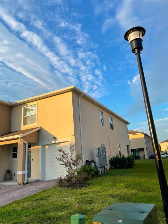 A tan two-story townhouse exterior with a garage and a tall street lamp nearby — 1485 ISLETA LOOP, KISSIMMEE, FL