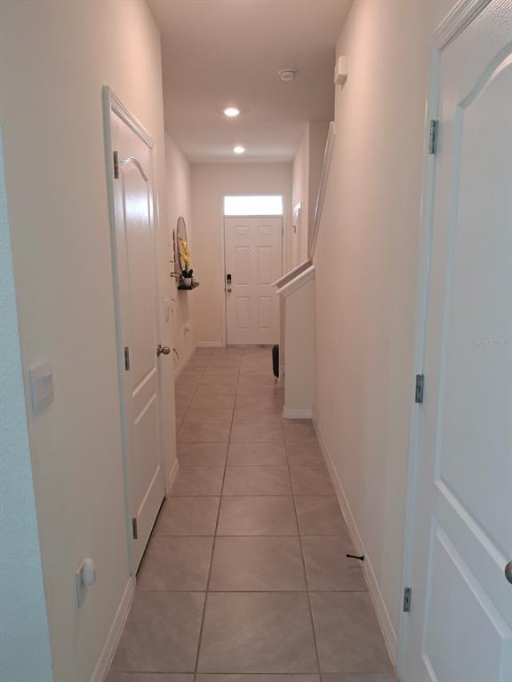 A hallway with light-colored tile flooring leads to a white front door — 1485 ISLETA LOOP, KISSIMMEE, FL