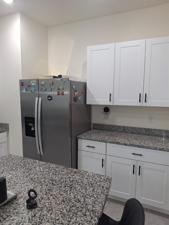 A kitchen features white cabinets, granite countertops, and a stainless steel side-by-side refrigerator — 1485 ISLETA LOOP, KISSIMMEE, FL