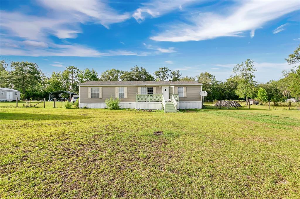 A single-story manufactured home sits on a large, grassy lot under a blue sky — 12531 NE 18TH STREET, WILLISTON, FL
